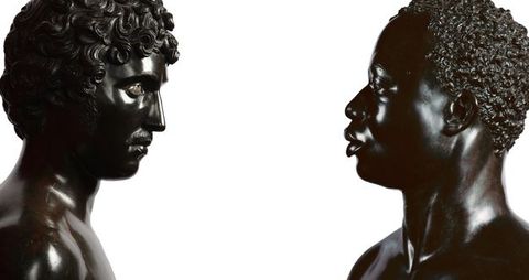 Photograph. From opposite ends of a long composition, two black stone busts face each other. To our left, Antico’s sculpture shows a person with full, curly hair, a straight nose, a moustache, and defined cheekbones. His chin is slightly tucked in. To our right, the face of Harwood’s sculpture seems to look levelly back. It depicts a Black man with short, curly hair, a softly curved nose, and full lips which are closed. Both are shown to the tops of their shoulders.