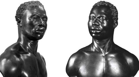 Photograph. Two carved, black stone busts include the heads, necks, and chests of almost identical Black men. Both have short, curly hair, noticeable eyebrow ridges, wide noses, and their full lips are closed. Tendons stand out in their necks, which turn halfway to profile. They have muscular shoulders and chests. One is angled to look off to our right, and the other to our left.