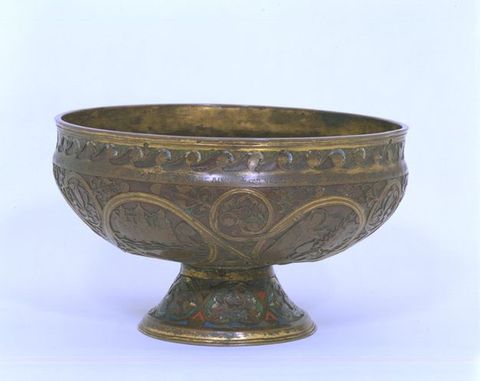 Ciborium. Metal vessel with a shallow bowl and wide rim sits on a low, flaring foot. Most of the metal is a darkened gold colour, but some areas are gilded with brighter gold. Scrolling lines enclose scenes and are filled in with leafy vines. A few touches of red, blue, and green enamel are visible on the foot.