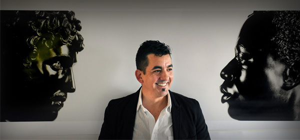 Installation photograph. From opposite ends of a long composition, profile views of two black stone busts face each other. To our left, Antico’s sculpture shows a person with full, curly hair, a straight nose, and defined cheekbones. His chin is slightly tucked in. To our right, the face of Harwood’s sculpture seems to look levelly back. It shows a Black man with short, curly hair, a softly curved nose, and full lips which are closed.