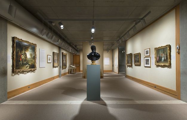 Photograph. Sculpted bust faces our right in profile against a deeply shadowed background. Light gleams off the polished bronze surface.