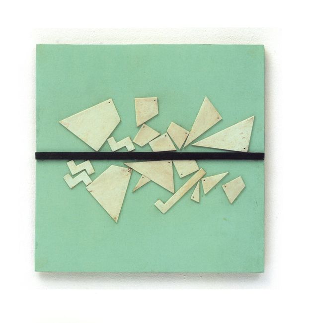 Assemblage. Thin, ivory-white, geometric pieces are nailed like a surreal and mismatched puzzle onto a cool green board. A black band spans the middle of the piece.