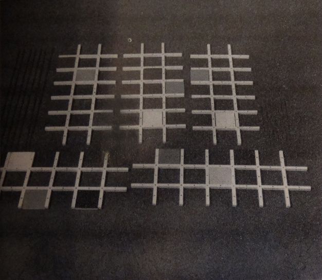 Sculpture. Six lattices, like pieces of a trellis, lie against a dark ground. Each is made of two long rows overlapping six shorter rows, like an elongated tic-tac-toe board. Each piece has one, two, or three cells filled in with solid squares in varying shades.