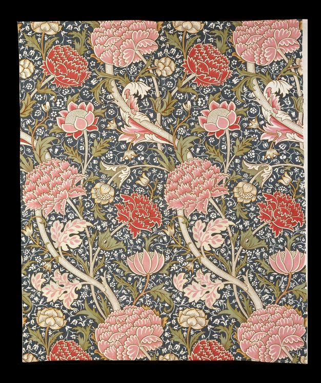 Textile. Petal-pink and red, stylized flowers grow on parchment-white stems with olive-green leaves to create a dense pattern. The background has a smaller pattern of white vines against deep blue.