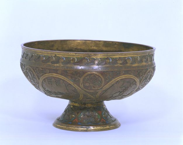 Ciborium. Metal vessel with a shallow bowl and wide rim sits on a low, flaring foot. Most of the metal is a darkened gold colour, but some areas are gilded with brighter gold. Scrolling lines enclose scenes and are filled in with leafy vines. A few touches of red, blue, and green enamel are visible on the foot.