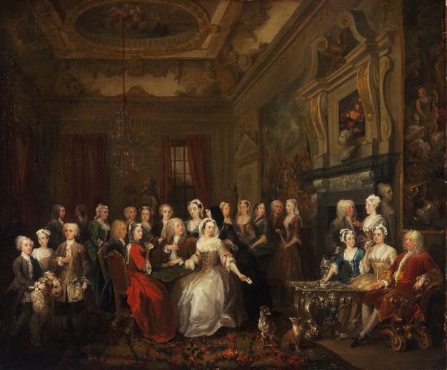 Painting. About two dozen men and women sit and stand around a hearth in a grand room elaborately decorated with moulding and painted plaster work. The women wear bonnets or lace caps and corseted dresses with long, shimmering skirts. The men wear white wigs and full suits with frilly cravats.