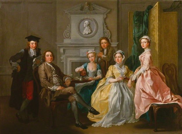 Painting. A man, woman, two younger men, and two younger women gather around a tea set on a round wooden table, placed in front of a hearth. They all have pale skin with rosy cheeks and pink lips. A profile portrait, carved like a cameo in grey, is in a medallion over the mantle.