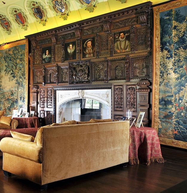 Carved woodwork. In this colour photograph of an interior, a wide, white-faced mantle is surrounded by intricately carved panels. Four painted portraits, including one of King Henry the Eighth, are set into the woodwork in a row along the top where the carved panels meet the ceiling.