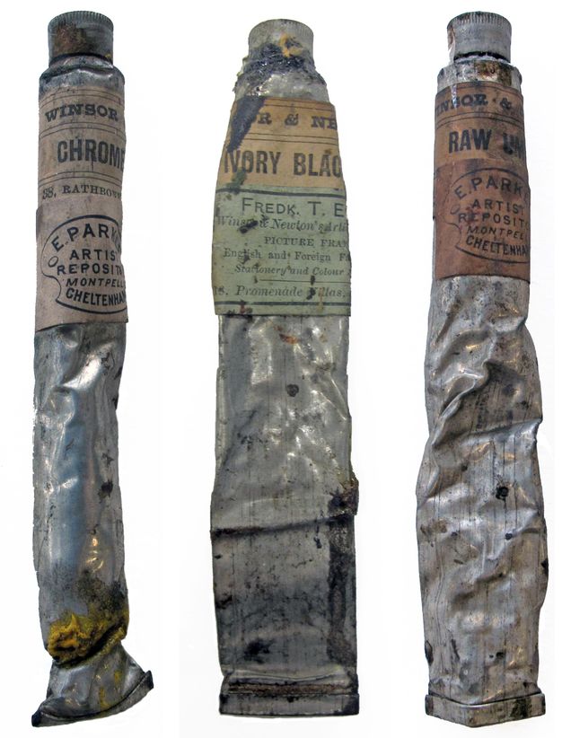 Three silver tubes of paint are partially crumpled. Each has a label near the top. From left to right, visible text reads “Winsor Chrome” on the first; “Ivory Black Fredk. T. E Winsor & Newton” at the centre; and “Windsor & Raw Um” to the right.