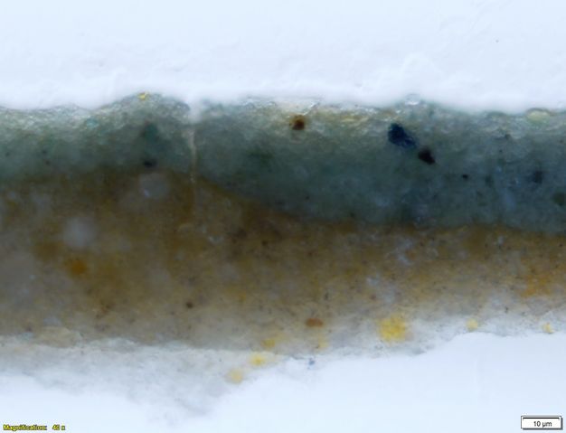Colour photograph. In this microscopic cross section of paint, a lower layer is flecked with yellow. The layer above is slate blue with a few specks of royal blue. Text in the lower left corner reads, “Magnification: 40x”, and in the lower right, “20µm”.