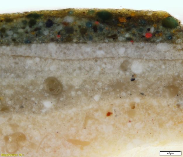 Colour photograph. In this microscopic cross section of paint, layers are pale straw yellow, then taupe and white. The uppermost layer is darker, speckled with red, blue, yellow, white, and black. Text in the lower left corner reads, “Magnification: 40x”, and in the lower right, “20µm”.