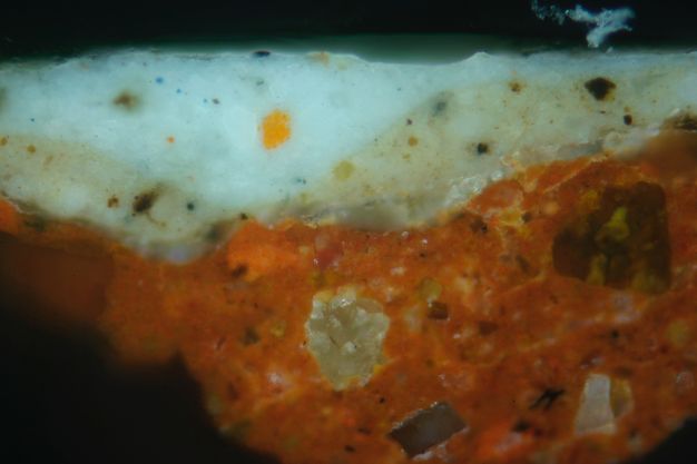 Colour photograph. In this microscopic cross section of paint, a layer of muted red is topped with a layer of florescent light blue.