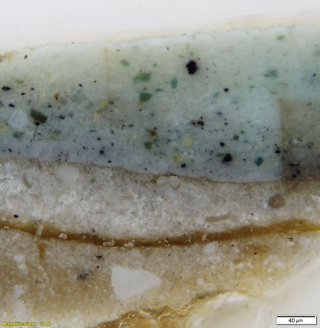 Colour photograph. In this microscopic cross section of paint, an ivory-white layer at the bottom is topped with a layer of brighter white and then faint grey with flecks of blue and green. Text in the lower left corner reads “Magnification: 20x”, and in the lower right corner, “40µm”.