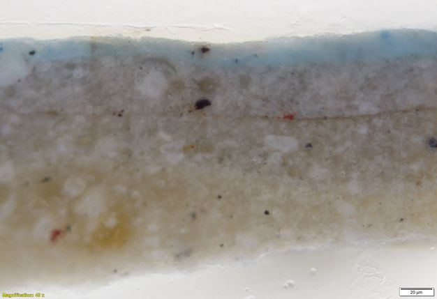 Colour photograph. In this microscopic cross section of paint, layers of grey and white are topped with a layer of pale blue. Text in the lower left corner reads, “Magnification: 40x”, and in the lower right, “20µm”.