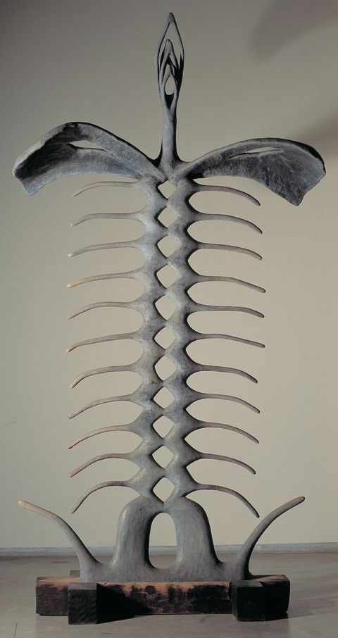 Sculpture. This freestanding metal sculpture is abstract but resembles the skeleton of an animal with a long spine and ribs like a fish. It sits on a wood base, and at the top, three nested marquise shapes unfold, like the arms of a dancer.