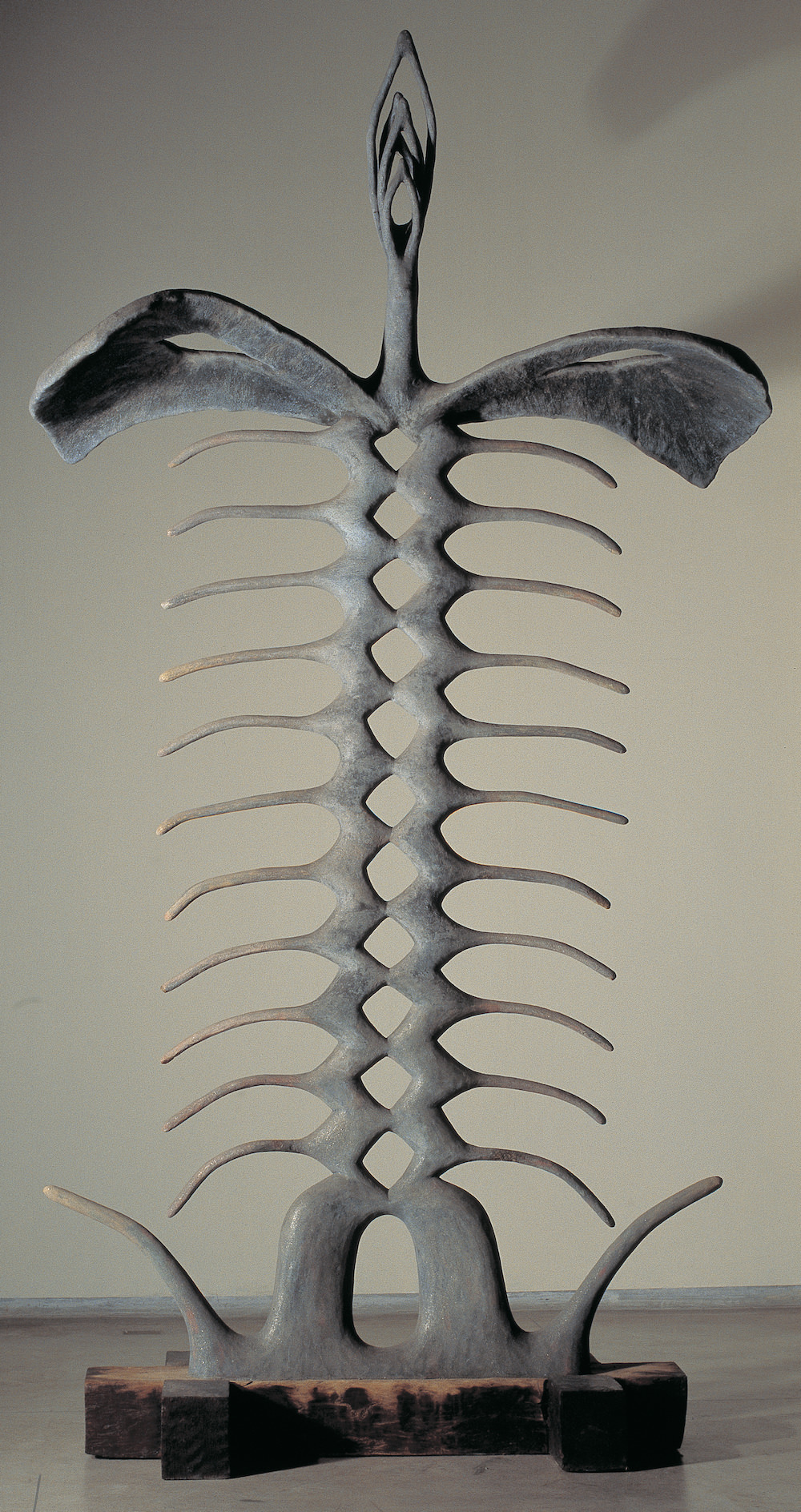 Sculpture. This freestanding metal sculpture is abstract but resembles the skeleton of an animal with a long spine and ribs like a fish. It sits on a wood base, and at the top, three nested marquise shapes unfold, like the arms of a dancer.