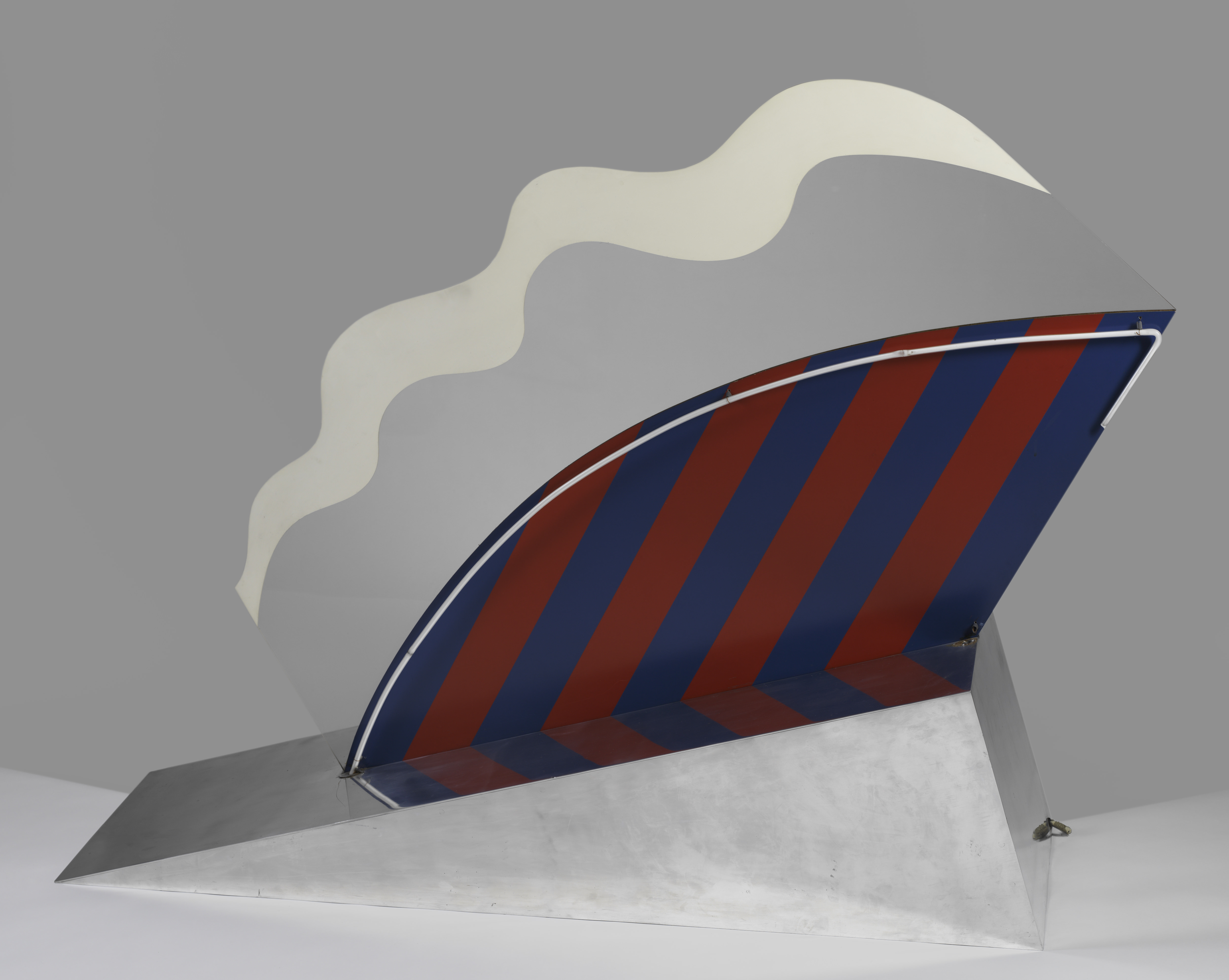 Sculpture. A silver wedge holds up an abstract, fan-shaped form. The bottom half of the fan is striped in navy blue and maroon red, and its curved upper edge is traced by a white neon tube. Above, bands of grey and white ripple like the edge of a pie crust.