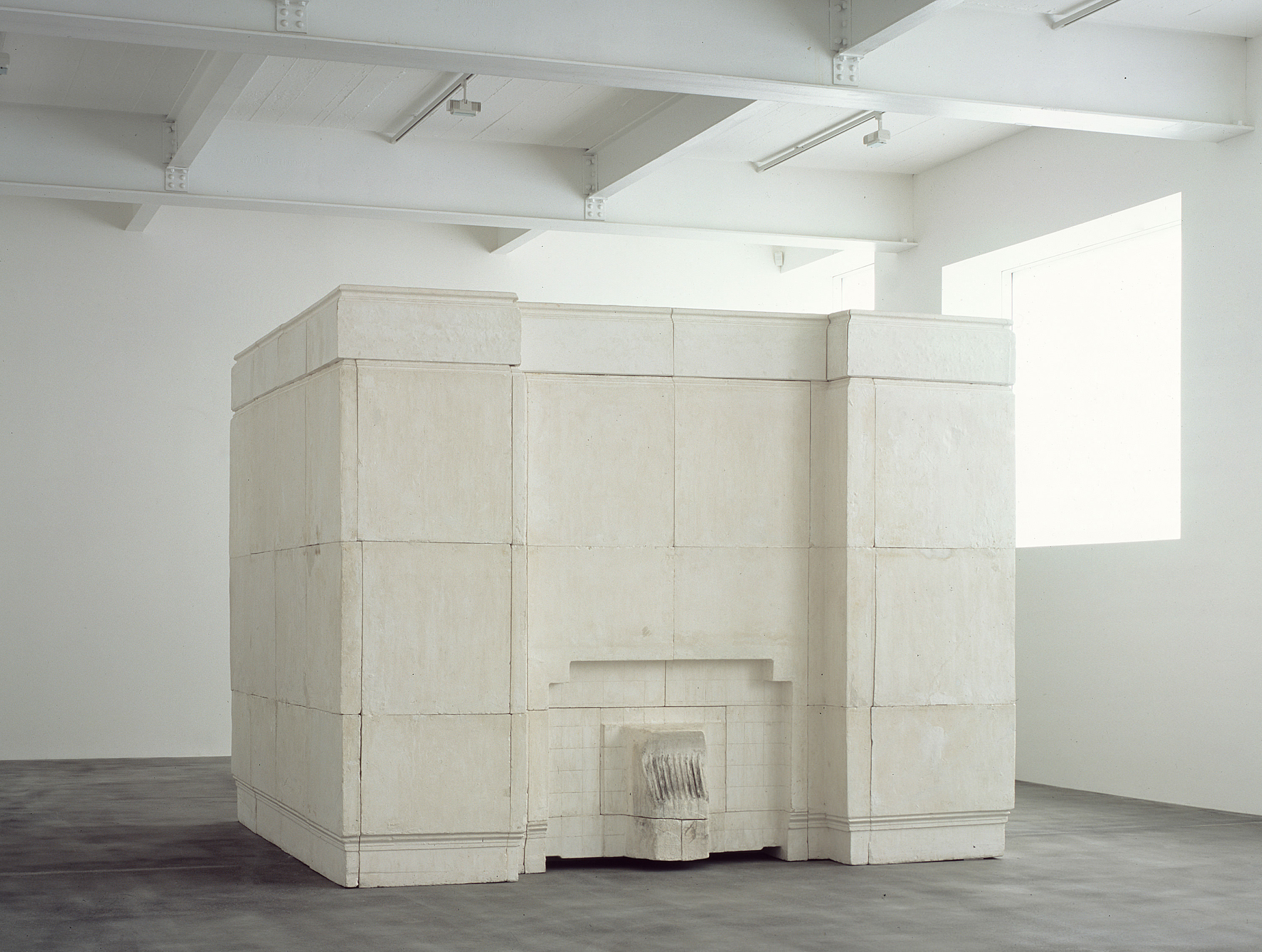 Sculpture. A plaster cast of the inside of a room with a fireplace nearly fills the gallery in which it is displayed. The work is constructed with plaster blocks. The tongue-like projection where the plaster filled the fireplace has traces of ash.