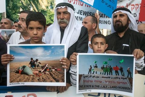 Colour photograph. Two boys hold up colour photographs at the head of a group holding signs in English and Hebrew. The people we can see have medium brown skin. The two men immediately behind the boys wear white gutrahs held in place by black, rope-like agals.