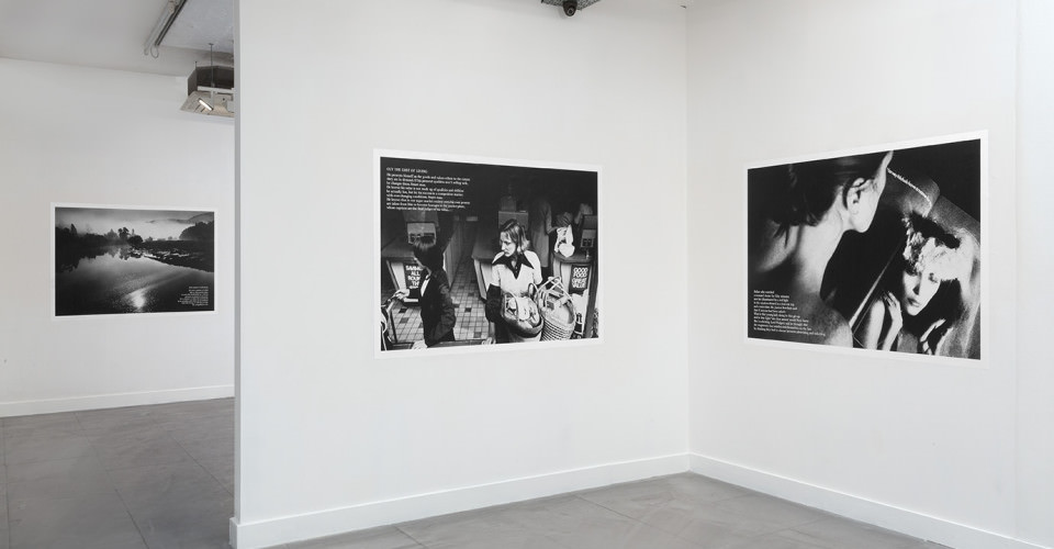 Installation photograph. Three black and white images are affixed to a gallery wall. White text is printed in a corner of each.