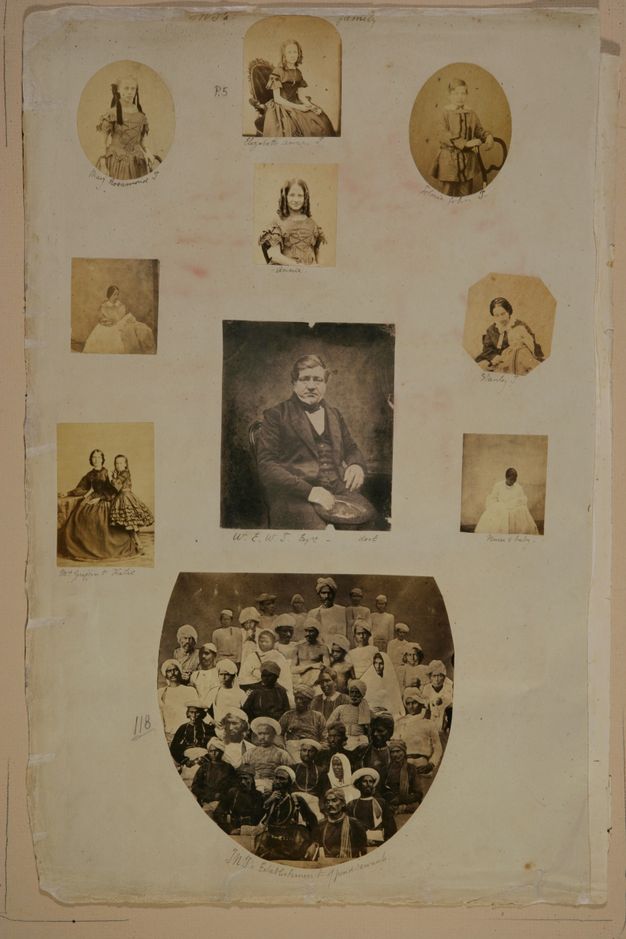 Page of a book. Of ten black and white photographs, seven are portraits of individuals, two show pairs of people, and the one at the bottom a group of about forty people. The photographs are rectangular, oval, octagonal, or arched. The centre photograph is of a man. Most of the rest are of women and children. Below, the group portrait shows darker-skinned people wearing turbans or caps.
