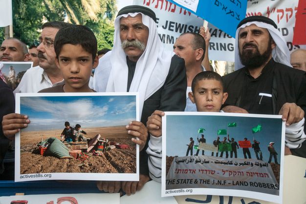 Colour photograph. Two boys hold up colour photographs at the head of a group holding signs in English and Hebrew. The people we can see have medium brown skin. The two men immediately behind the boys wear white gutrahs held in place by black, rope-like agals.