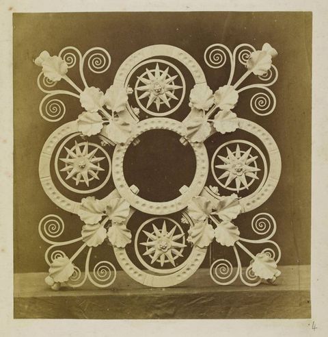 Metalwork. Printed in sepia-brown tones, a light-coloured, ornamental spandrel has four lobes. Each lobe is filled with a starburst overlapping a spiral. More ironwork curls like impossibly perfect tendrils from where the lobes meet.