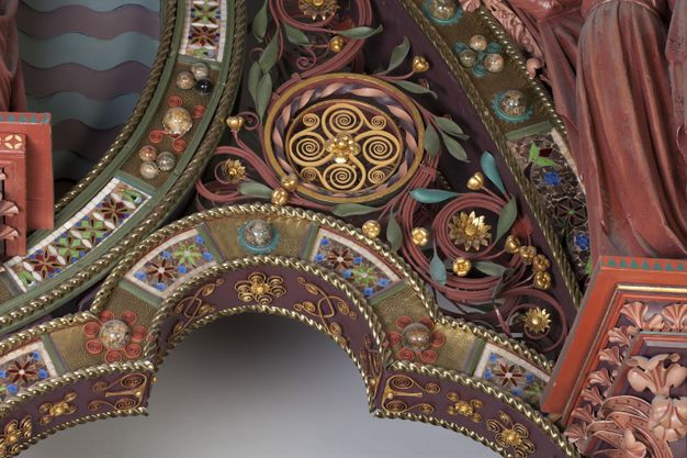Choir screen. Detail view of varied ornamentation: jewel-toned scrolls, filigree, flowers, and patterns over one of the bays of a choir screen. Much of the metal work spirals tightly, like paper quilling. The flat surfaces are set with glass and round stones.
