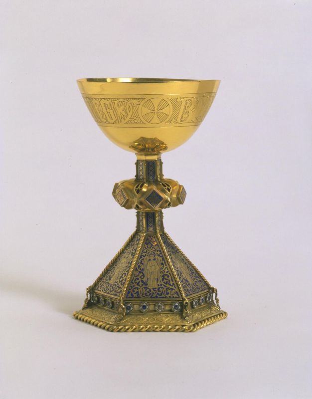 Chalice. A shiny gold rounded cup sits on a stem with a thick, jewelled ring around its centre. The eight-sided foot that flares beneath is as tall as the stem and cup, and it is enamelled with blue and gold.