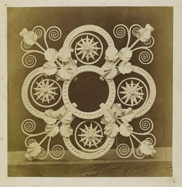 Metalwork. Printed in sepia-brown tones, a light-coloured, ornamental spandrel has four lobes. Each lobe is filled with a starburst overlapping a spiral. More ironwork curls like impossibly perfect tendrils from where the lobes meet.