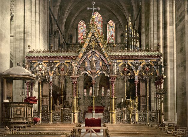 Choir screen. Spanning the width of a nave, this partition has five bays, each under a pointed arch. Each arch is then bisected by a spindly column. The central bay is the widest and tallest, and a person stands at its apex. Intricate tracery encrusts the upper edges of the screen and fills in the arches. Panels across the bottom are also made with intricately patterned tracery. Most surfaces are shiny or burnished gold, and there are also touches of muted red, warm yellow, and earthy green.