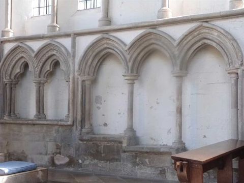 Architecture. Three pointed arches outlined in grey stone against a white wall create three niche-like spaces. A wide ledge below steps down in each successive niche, resulting in seats at three levels.