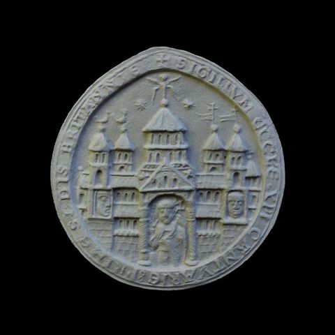 Seal. Cast of a round seal shows a church with five towers over a porch with a triangular pediment. A figure stands beneath the pediment. Two faces, one to each side, are in niches under towers at either end of the building. Latin text lines the perimeter.
