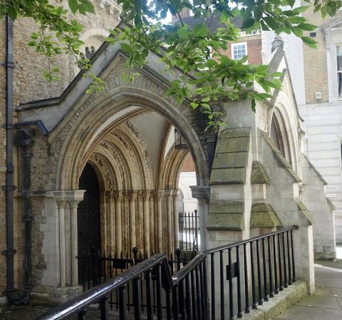 Architecture. An arched stone porch extends from an arched doorway, which is lined with the nested arches of the archivolt on the side of a church. The porch has a slightly pointed arch on the side we see the most clearly.