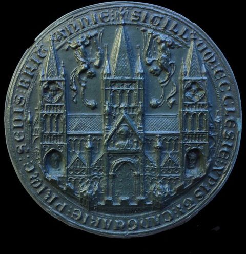 Seal. Cast of a round seal shows a church with three towers. Facing head-down, winged angels blow horns between the towers. Latin text lines the perimeter.