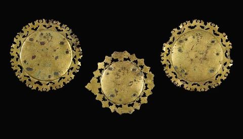 Plaques. The backs of three medallion-like roundels with decorated perimeters are shiny gold with a few dark spots.