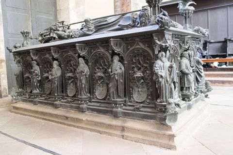 Sculpture. The sides of this rectangular bronze tomb are decorated with arches filled with tracery and heraldic crests. Between each arch and the next is a figure standing on a hexagonal platform under a miniature canopy. Those on the sides facing us appear to be all men wearing robes, and they hold one or two objects. They have curly or wavy hair, and most have full beards. We are low to the ground so only catch a glimpse of the figure on the top of the tomb.