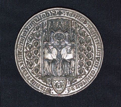 Seal. In this round seal, an enthroned man, God the Father, holds a crucifixion. Twenty miniature heads, ten to each side, are encircled with continuous vines sprouting near a coat of arms. Gothic writing runs around the perimeter, in reverse.