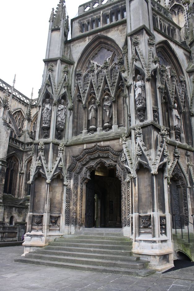 Architecture. A lavishly carved and ornamented porch extends from the side of a stone Church. Stairs lead up to the opening which is arched, but segmented into three, bracket-like lobes.