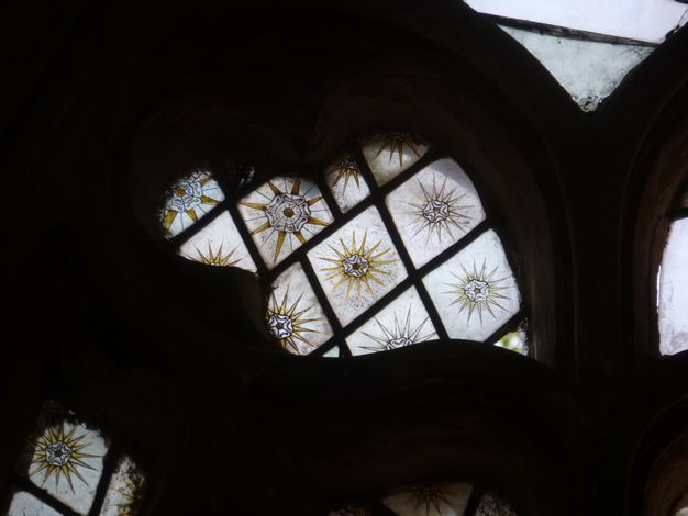 Stained glass window. Detail view of a leaf-shaped opening for stained glass. Diamond-shaped panes have gold sunbursts overlaid with stylized white roses.