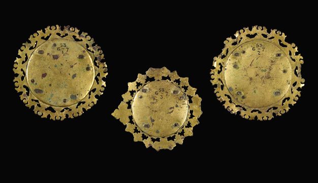 Plaques. The backs of three medallion-like roundels with decorated perimeters are shiny gold with a few dark spots.