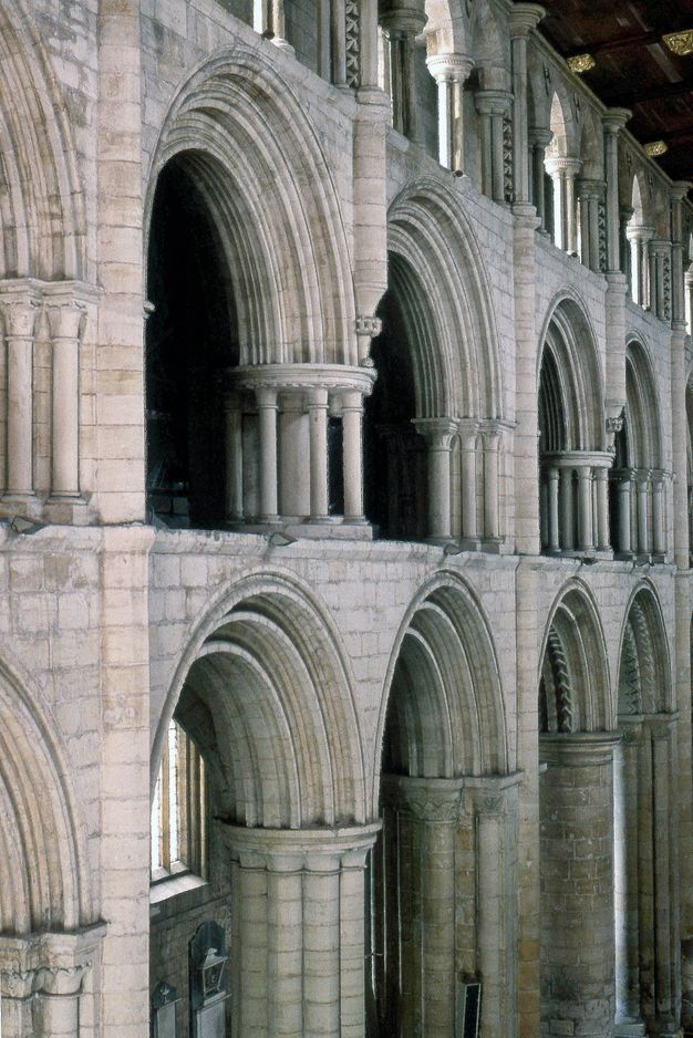 Architecture. Three levels of stone arches angle away from us to our right in this church interior. The middle, gallery level has rings of disengaged columns around supporting piers between the rounded arches.