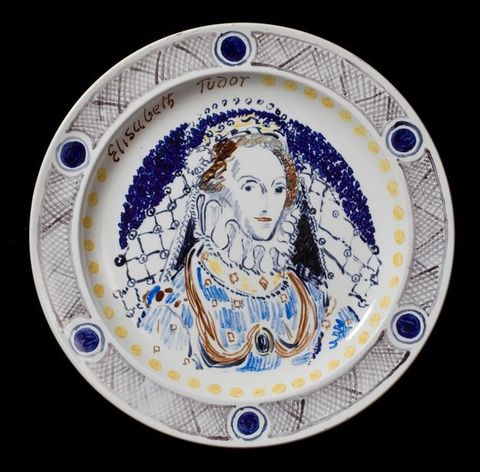 Plate. A woman wearing a crown and a high, ruffled collar looks sideways at us. A veil falls from the back of her crown to her jewelled dress. The portrait is painted mostly in tones of blue with some touches of brown, black and yellow. A ring of yellow dots runs just inside the rim of the plate, and her name is painted at the upper left, \“Elisabeth Tudor\”.