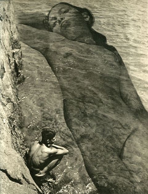 Photogravure. We look down at a calm sea lapping at steep cliffs. A boy squats on what appears to be a natural stone ledge by the water’s edge and peers into the water. At a much larger scale, a young woman’s nude, prone body is overlaid in the water so it spans the height of the picture.