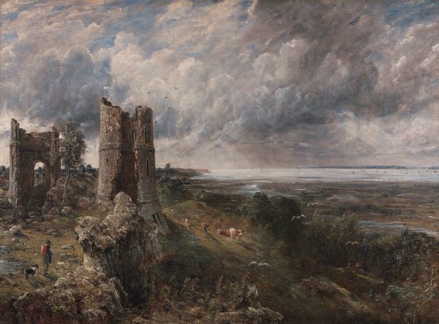 Painting. The ruins of a building and its tower, to our left, perch at the edge of a slope that leads down to a low plane and then to a wide expanse of water to our right. A person and dog walk near the lower left corner of the canvas, and another person tends three cows near the tower. The horizon comes just under halfway up the composition. Rays of sunlight angle down out of pale grey, blue, and white clouds above.