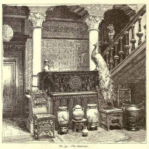 Illustration. Porcelains and a stuffed peacock are arranged in front of and on a low wall leading to a staircase with heavily carved spindles. Columns hold up a panelled ceiling, and the wall behind is covered with patterned paper or cloth.