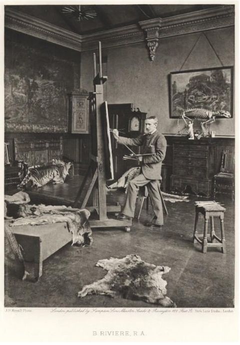 Photogravure. A man wearing a suit stands painting at an easel that nearly reaches the high ceiling. Animal skins drape over furniture and lie on the floor. An animal’s skeleton stands on a piece of furniture on the far wall.