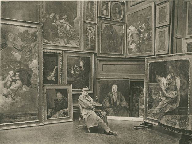 Photogravure. A pale-skinned man wearing a painter’s coat and holding a palette sits near the corner of a room hung frame-to-frame with paintings. More paintings lean against the wall from the floor. The works are of portraits, religious scenes, and genre scenes.