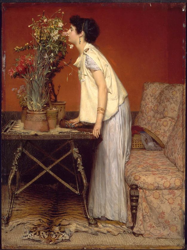 Painting. A dark-haired, pale-skinned woman leans onto a table to smell tall potted flowers. The table’s metal legs pin a tiger’s pelt underfoot. A floral-patterned couch is to our right. The wall behind the woman is terracotta red above and black below.