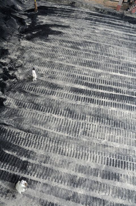 The tracks of a bulldozer’s wheels are imprinted in grey stone dust. We look down on the prepared ground, which resembles rows of zipper teeth. Three people on the ground are miniscule in scale.